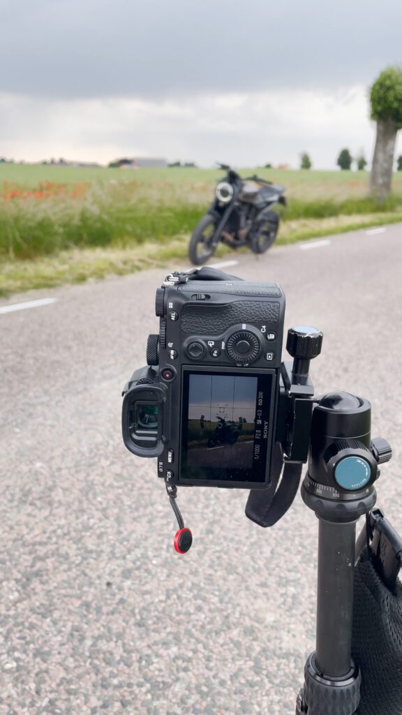 A camera set up on a tripod capturing a photo of a motorcycle parked by the side of a scenic road.