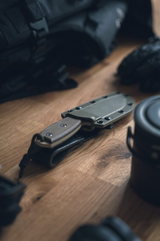 A camping knife in its protective sheath, resting on a wooden floor.